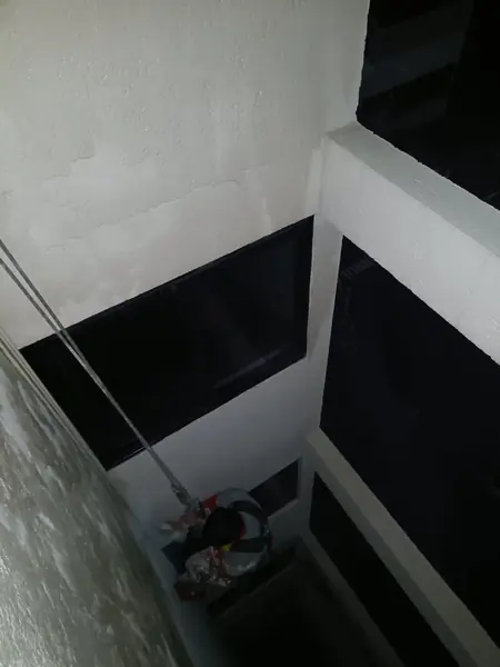 Vista en picada de un patio interior con ventanas oscuras, cuerdas y un trabajador suspendido en un nivel inferior.