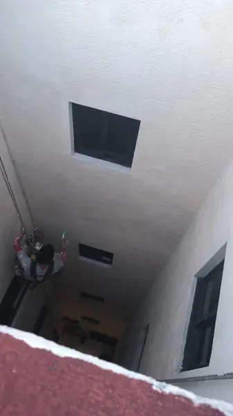 Patio interior visto desde un borde de azotea, con un trabajador suspendido a la izquierda que sostiene un atomizador junto al muro.
