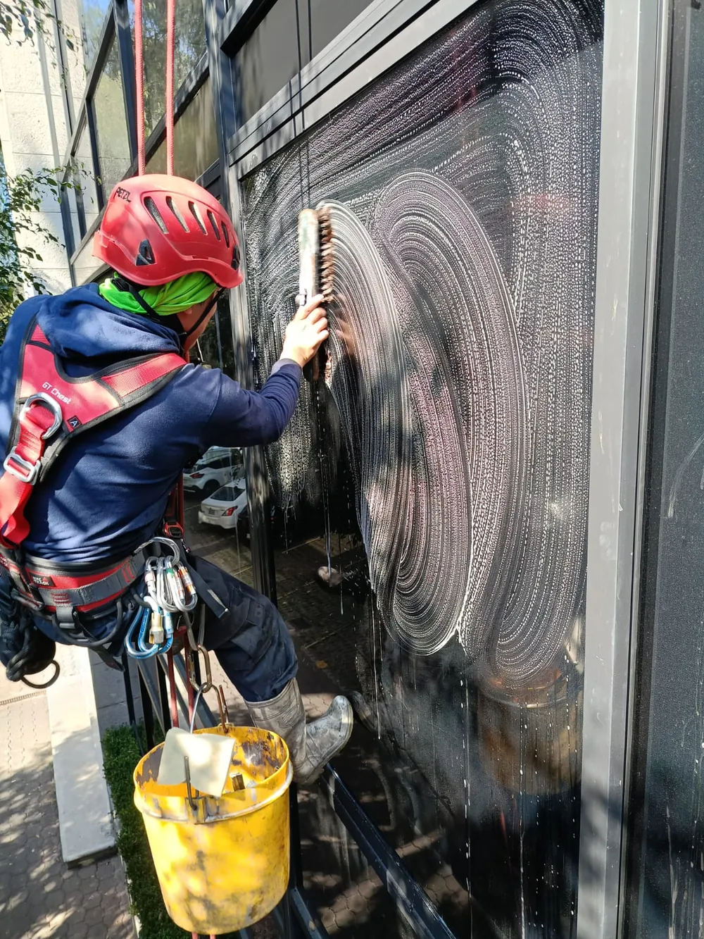 Operario con casco y arnés limpiando un vidrio mediante acceso por cuerdas.