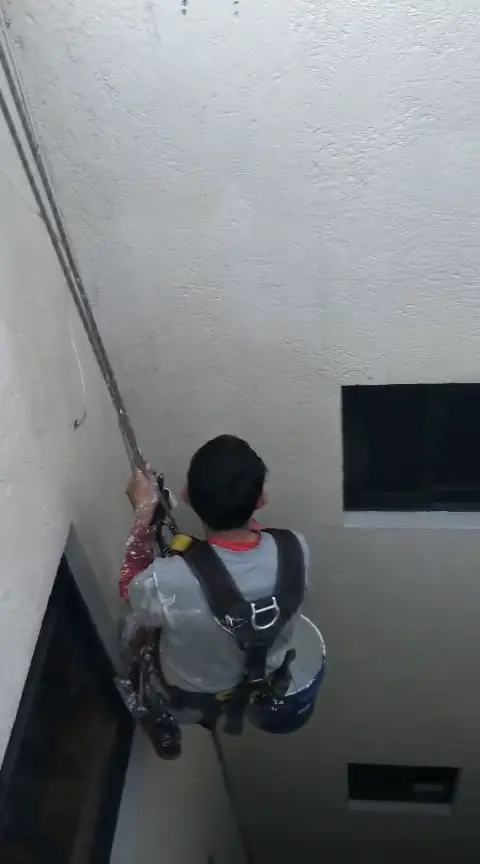 Operario suspendido ante muros blancos y ventanas de un patio interior.