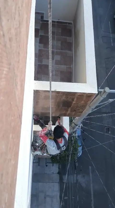 Operario suspendido por cuerdas debajo de un balcón, frente al muro exterior.