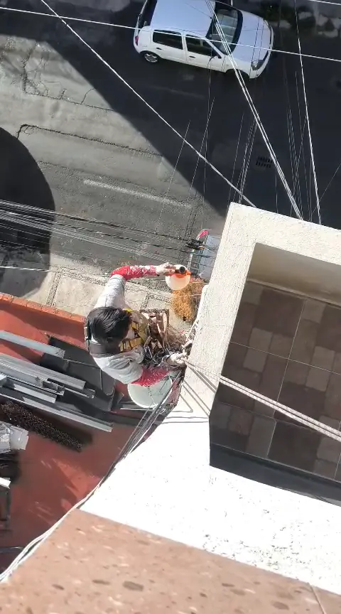Operario con arnés y cuerdas manipulando un rociador manual junto a la esquina exterior de la fachada.